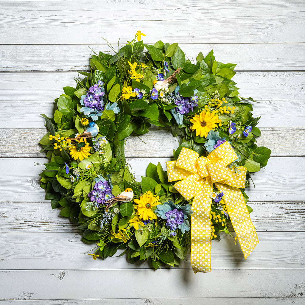 Fresh salal and sweet huckleberry with faux lavender pansies, faux yellow forsythia flowers, faux purple delphinium flowers, faux yellow daisies, and three birds with a yellow polka-dot bow