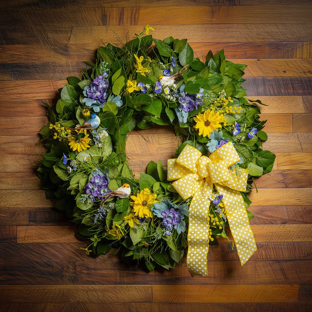 Fresh salal and sweet huckleberry with faux lavender pansies, faux yellow forsythia flowers, faux purple delphinium flowers, faux yellow daisies, and three birds with a yellow polka-dot bow