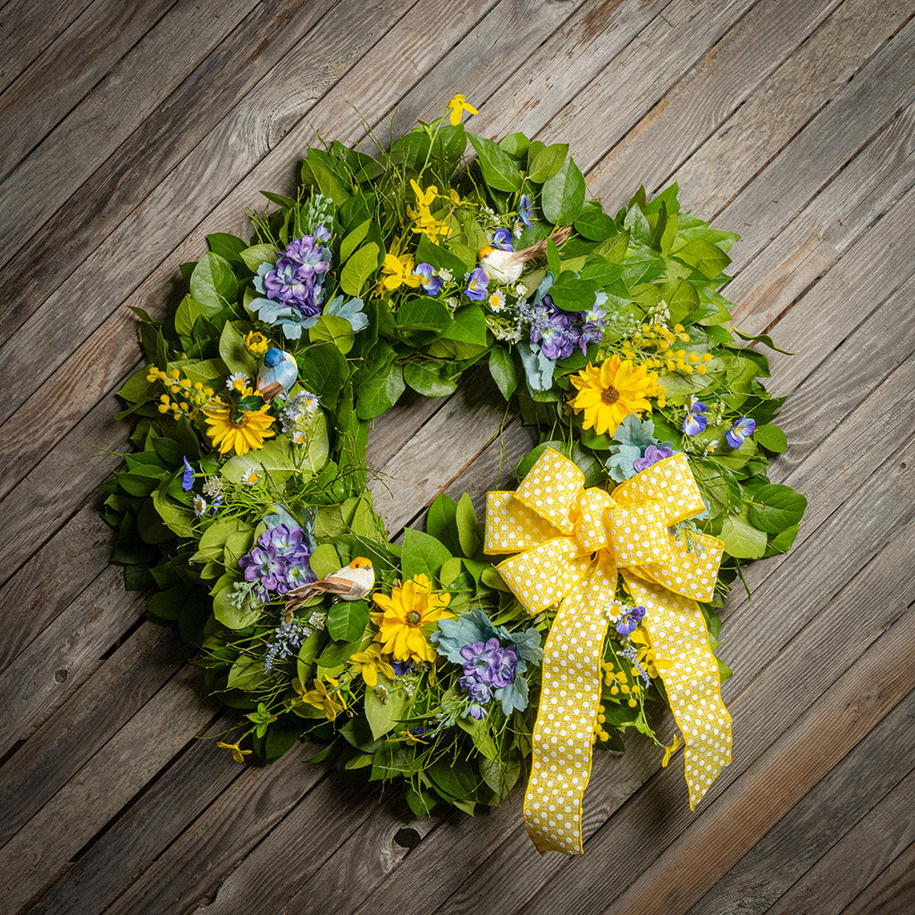 Fresh salal and sweet huckleberry with faux lavender pansies, faux yellow forsythia flowers, faux purple delphinium flowers, faux yellow daisies, and three birds with a yellow polka-dot bow