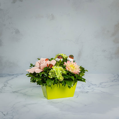 Fresh salal and green huckleberry with faux green hydrangeas, faux pink dahlia, two chickadee birds, and a peach-striped linen bow in a green container