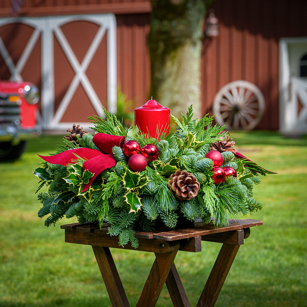 Christmas centerpiece with holly, pine cones, red ornaments and a red pillar candle