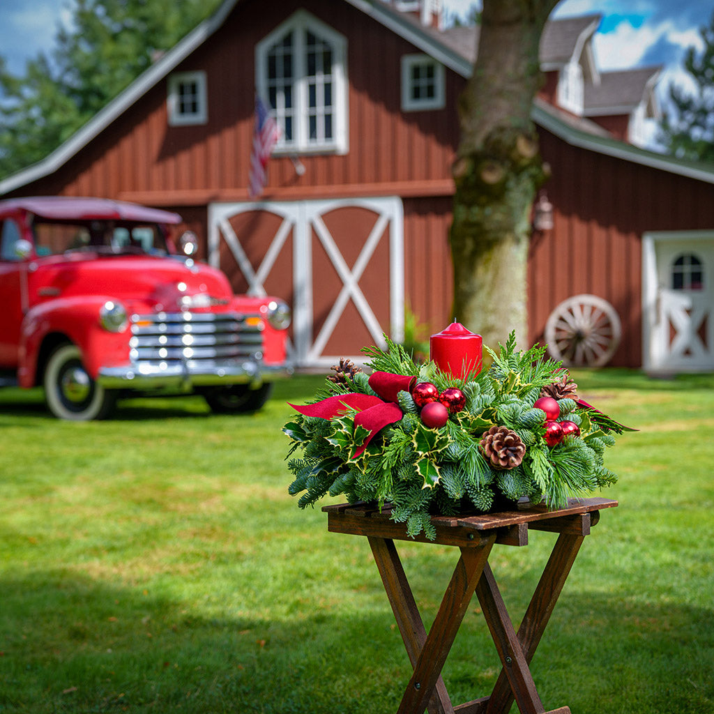 Christmas centerpiece with holly, pine cones, red ornaments and a red pillar candle