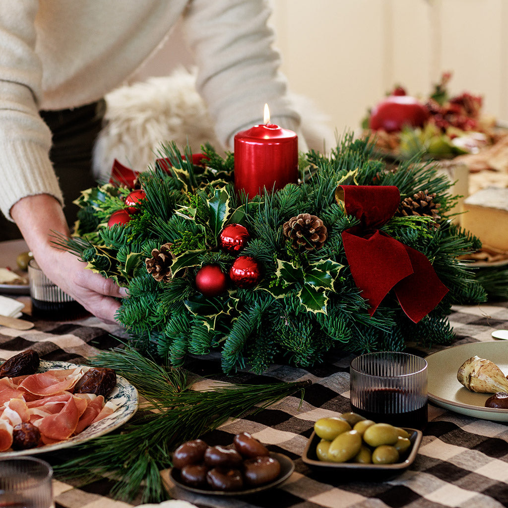 Christmas centerpiece with holly, pine cones, red ornaments and a red pillar candle on a table