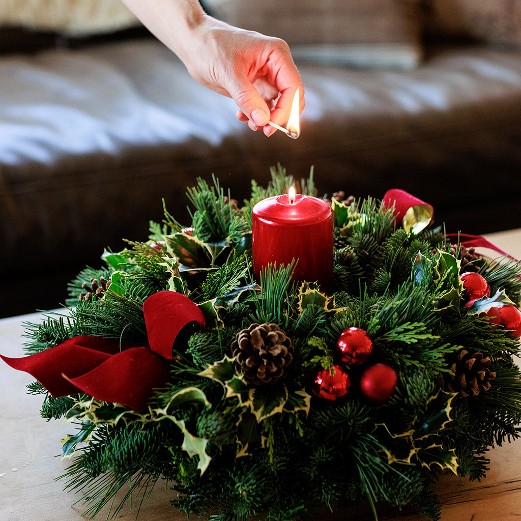 Christmas centerpiece with holly, pine cones, red ornaments and a red pillar candle