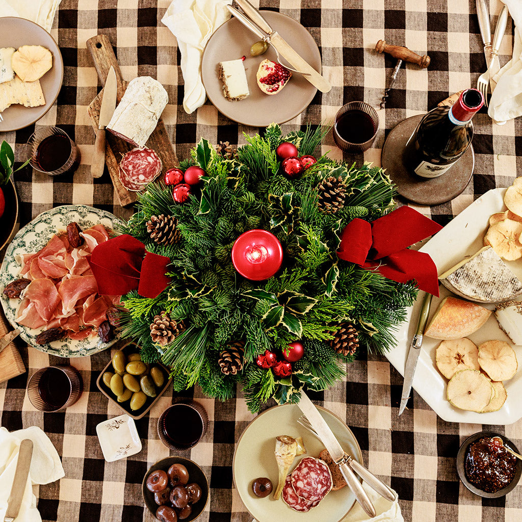 Christmas centerpiece with holly, pine cones, red ornaments and a red pillar candle on a table