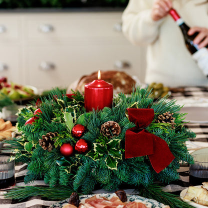 Christmas centerpiece with holly, pine cones, red ornaments and a red pillar candle