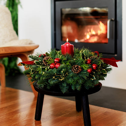 Christmas centerpiece with holly, pine cones, red ornaments and a red pillar candle