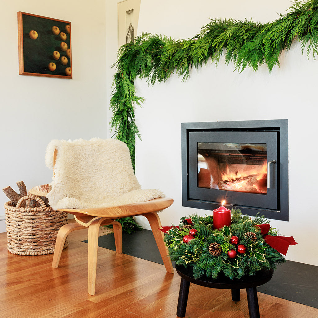 Christmas centerpiece with holly, pine cones, red ornaments and a red pillar candle