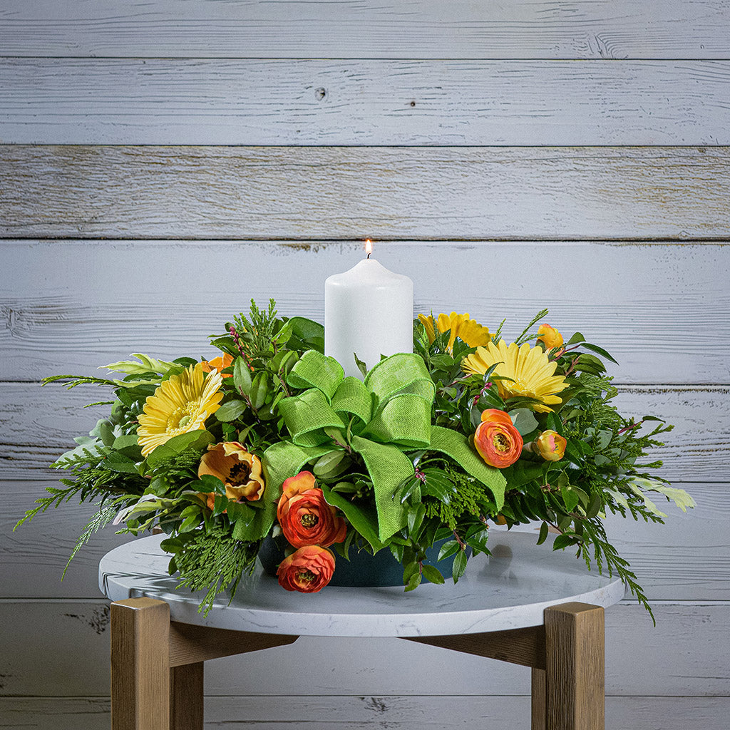 Floral arrangement with a white candle on a wooden table against a wooden wall.