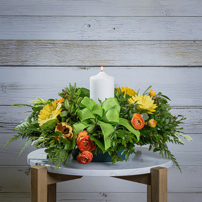 Floral arrangement with a white candle on a wooden table against a wooden wall.
