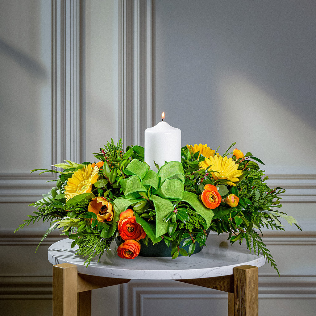 Floral arrangement with a white candle on a marble surface against a gray wall.