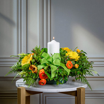 Floral arrangement with a white candle on a marble surface against a gray wall.