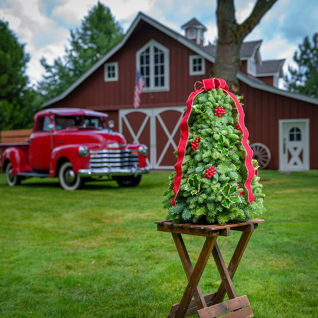 Fresh hand-assembled tabletop Christmas tree with fir, variegated holly, red berries and a red velveteen bow and white LEDs