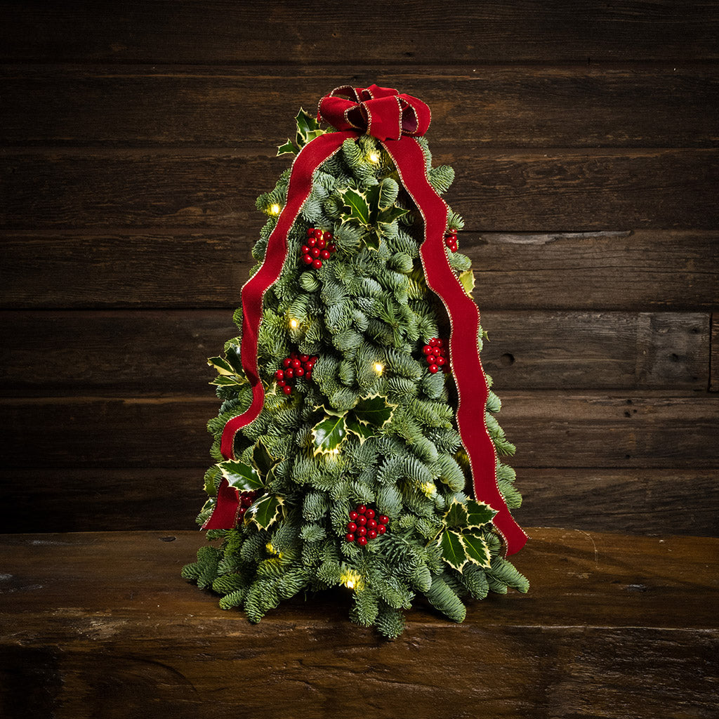 Fresh hand-assembled tabletop Christmas tree with fir, variegated holly, red berries and a red velveteen bow and white LEDs