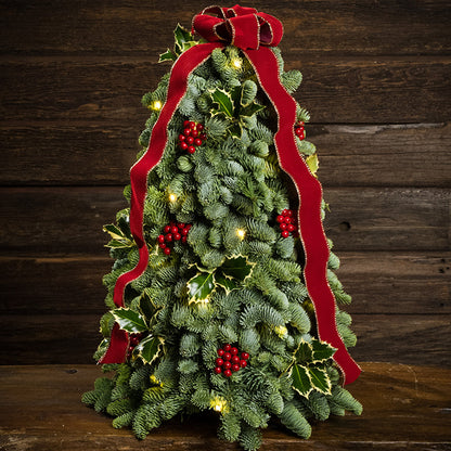 Fresh hand-assembled tabletop Christmas tree with fir, variegated holly, red berries and a red velveteen bow and white LEDs