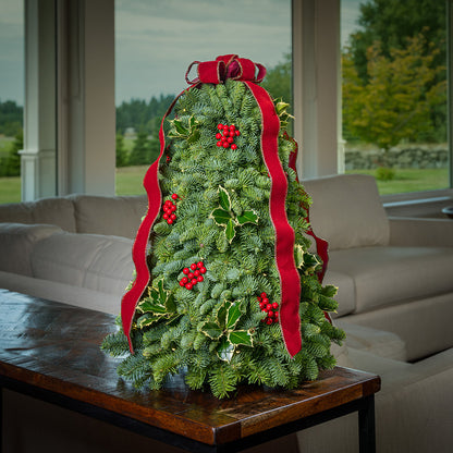 Fresh hand-assembled tabletop Christmas tree with fir, variegated holly, red berries and a red velveteen bow and white LEDs