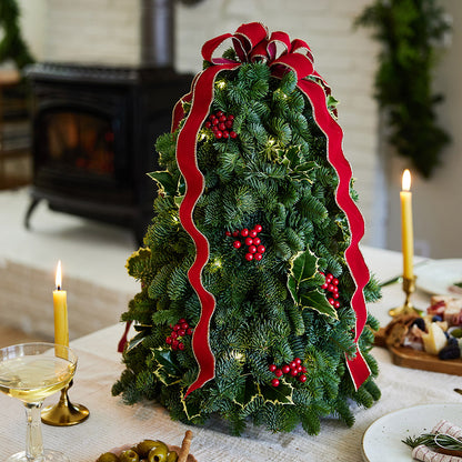 Fresh hand-assembled tabletop Christmas tree with fir, variegated holly, red berries and a red velveteen bow and white LEDs