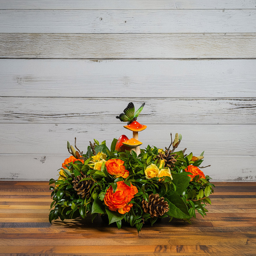 Fresh salal and green huckleberry with faux mini yellow roses, faux orange ranunculus flowers, faux magnolia branches, natural pinecones, and a resin mushroom & butterfly decoration