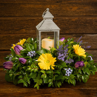 Fresh salal and green huckleberry with faux yellow gerbera daisies, faux purple tulips, faux lavender, and faux purple berries with a gray LED lantern