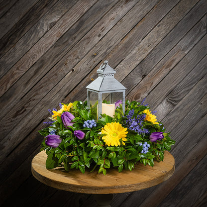 Fresh salal and green huckleberry with faux yellow gerbera daisies, faux purple tulips, faux lavender, and faux purple berries with a gray LED lantern