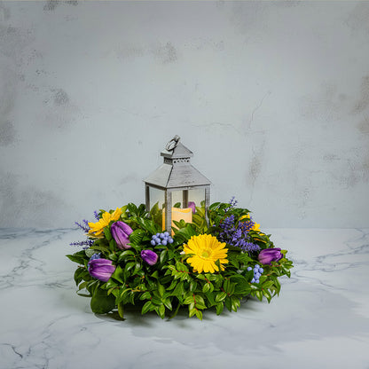 Fresh salal and green huckleberry with faux yellow gerbera daisies, faux purple tulips, faux lavender, and faux purple berries with a gray LED lantern