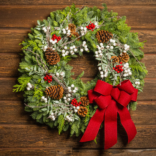 Christmas wreath with greenery, pinecones, berries, and a red bow on a wooden background