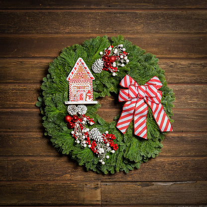 Gingerbread house with red and white decorations and red and white striped bow on evergreen wreath