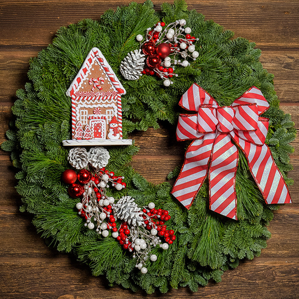 Gingerbread house with red and white decorations and red and white striped bow on evergreen wreath