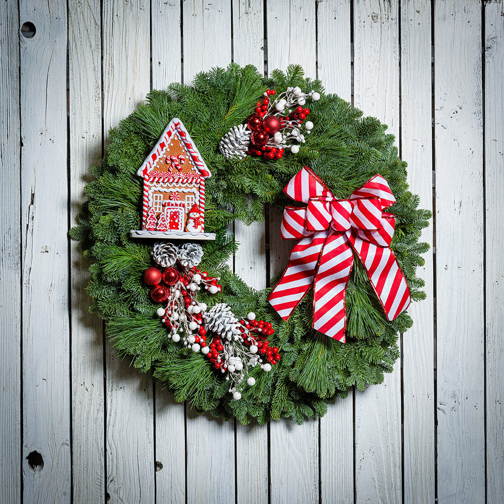 Gingerbread house with red and white decorations and red and white striped bow on evergreen wreath