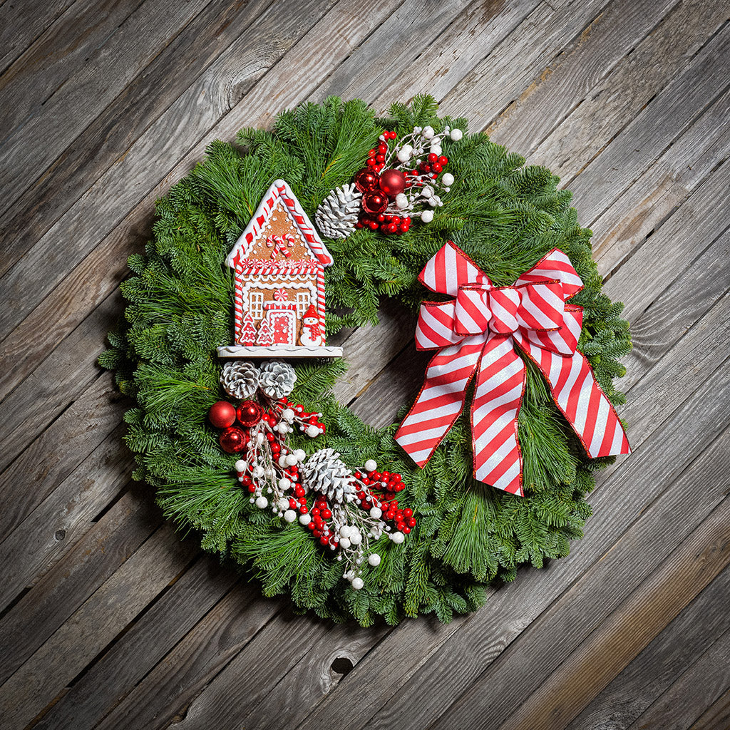 Gingerbread house with red and white decorations and red and white striped bow on evergreen wreath