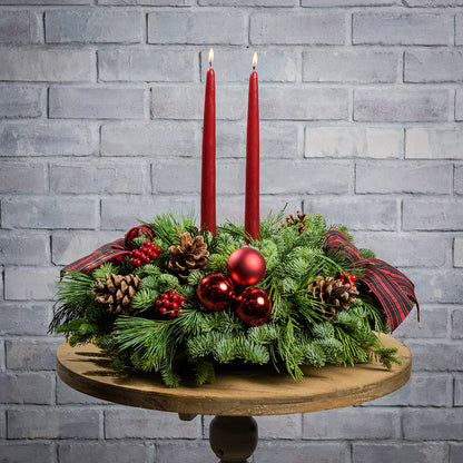 Evergreen arrangement of noble fir, cedar, and white pine with faux red berries, red ball ornaments, natural pinecones, plaid bows, and two red taper candles