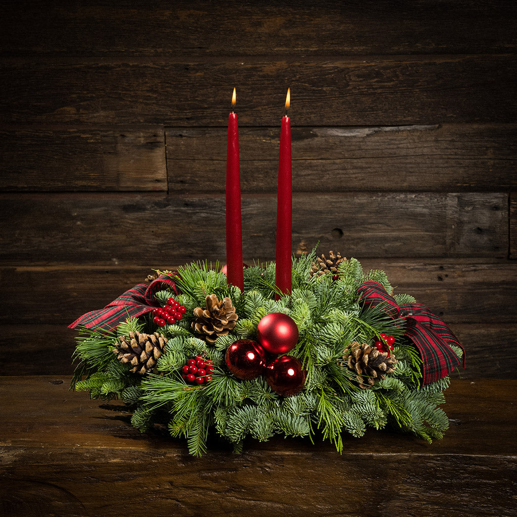 Evergreen arrangement of noble fir, cedar, and white pine with faux red berries, red ball ornaments, natural pinecones, plaid bows, and two red taper candles