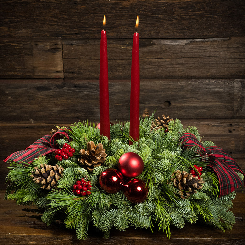 Evergreen arrangement of noble fir, cedar, and white pine with faux red berries, red ball ornaments, natural pinecones, plaid bows, and two red taper candles