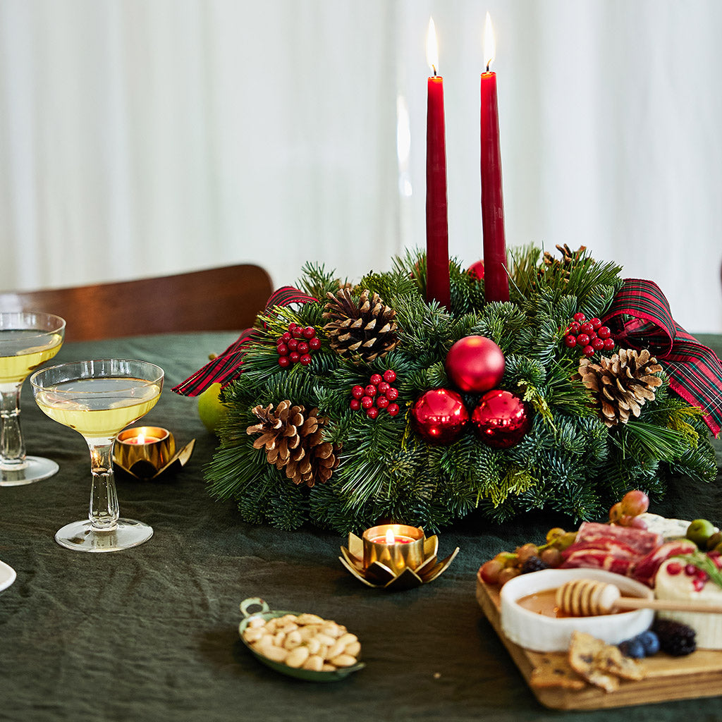 Evergreen arrangement of noble fir, cedar, and white pine with faux red berries, red ball ornaments, natural pinecones, plaid bows, and two red taper candles