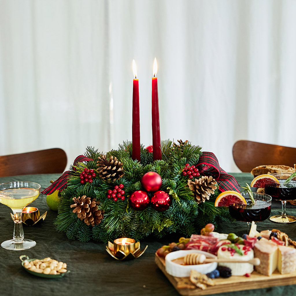 Evergreen arrangement of noble fir, cedar, and white pine with faux red berries, red ball ornaments, natural pinecones, plaid bows, and two red taper candles