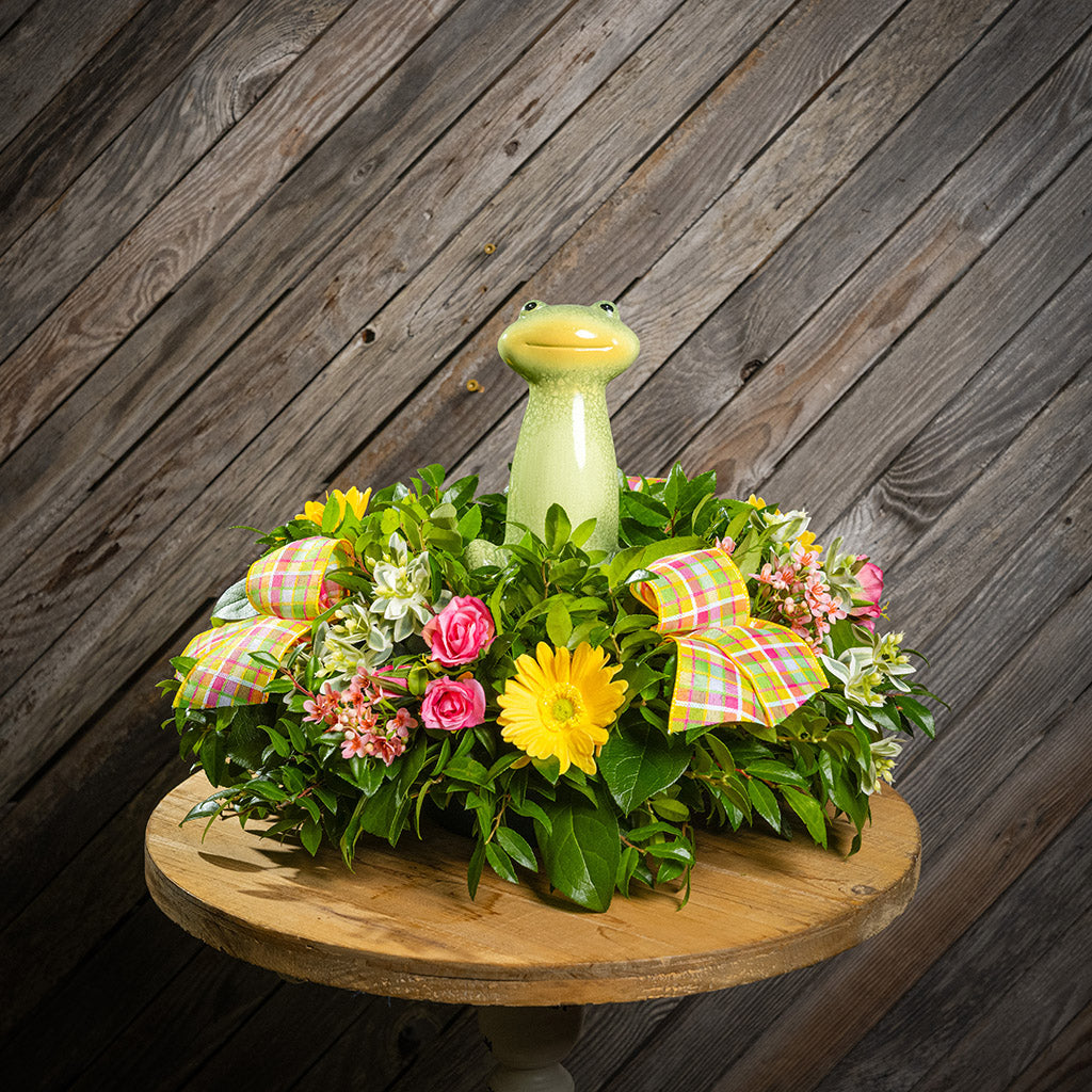 Fresh salal and green huckleberry with faux yellow daisies, faux pink wax flowers, faux mini roses, faux variegated greens, plaid bows, and a ceramic frog decoration