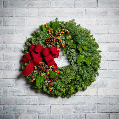 Holiday wreath with pine cones, faux autumn berries and a red linen bow on a base of noble, pine and salal greens