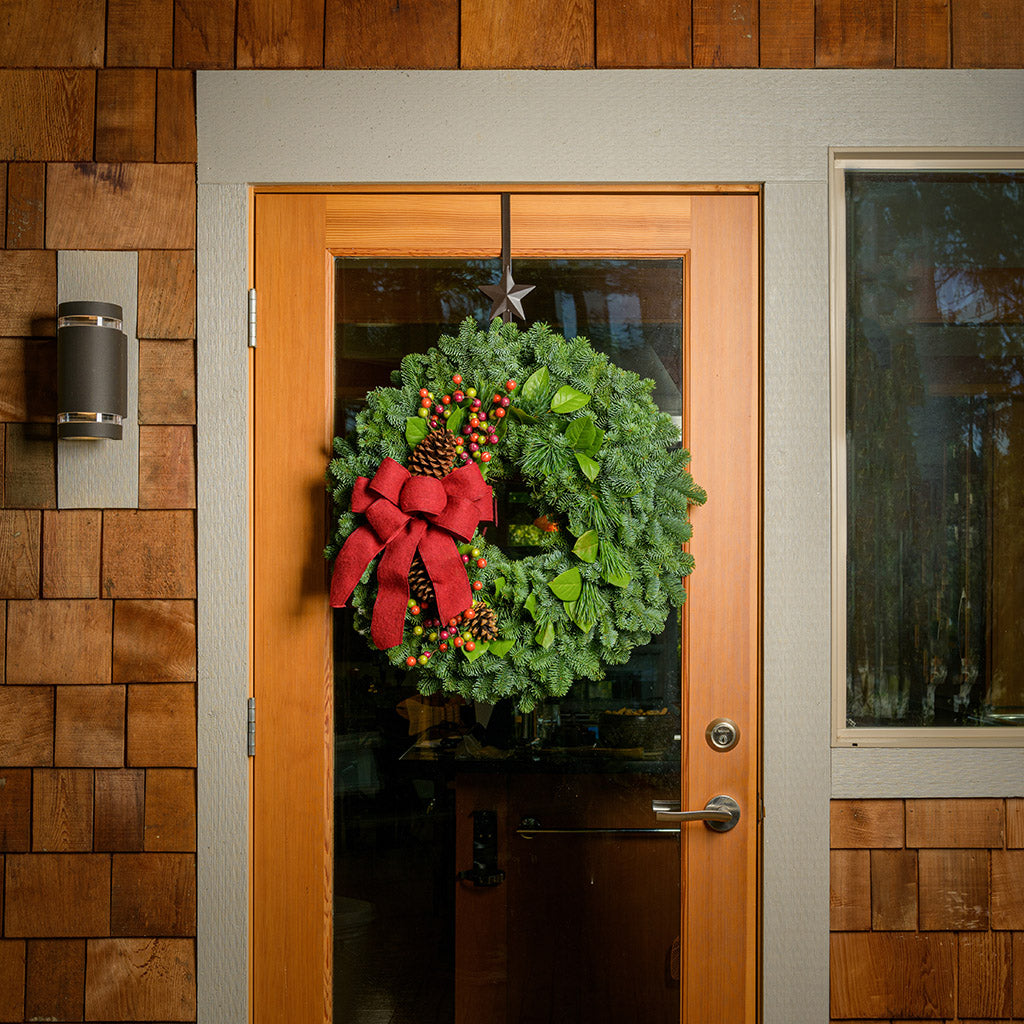 Holiday wreath with pine cones, faux autumn berries and a red linen bow on a base of noble, pine and salal greens