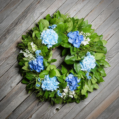 Floral wreath with blue flowers and green leaves on a wooden surface