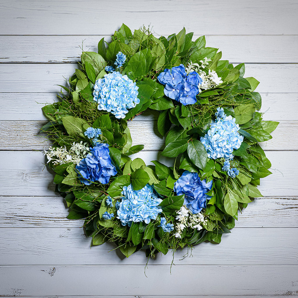Wreath with blue flowers and green leaves on a wooden background