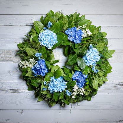 Wreath with blue flowers and green leaves on a wooden background