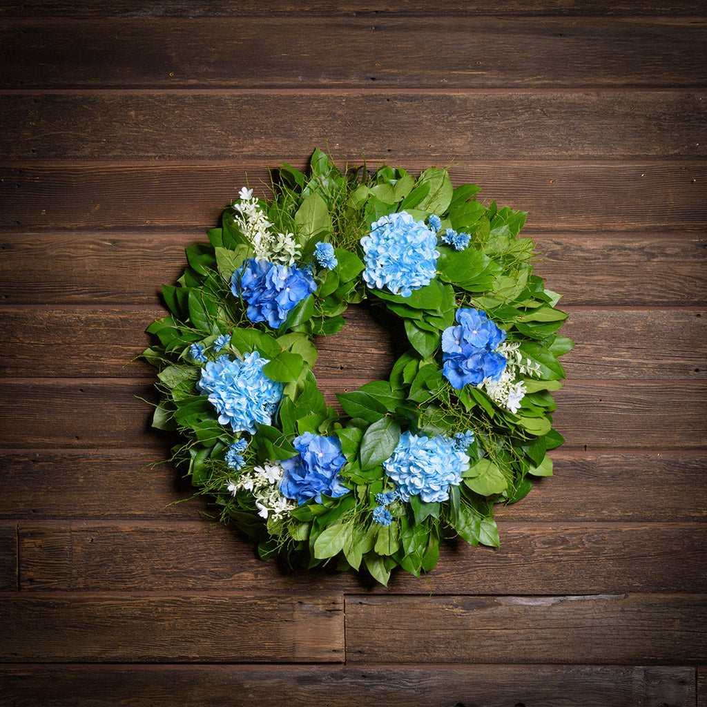 Floral wreath with blue flowers and green leaves on a wooden background