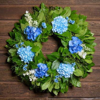 Floral wreath with blue flowers and green leaves on a wooden background
