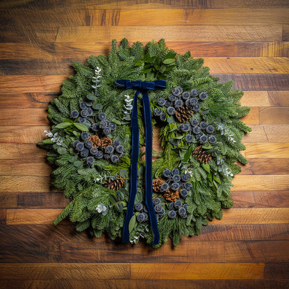 Green wreath with pinecones and a blue ribbon on a wooden surface