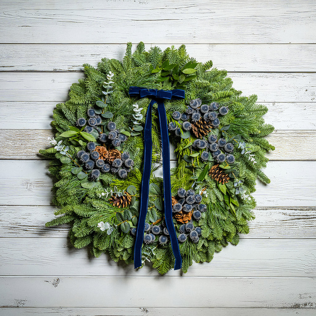 Christmas wreath with greenery, pinecones, and a blue ribbon on a wooden background