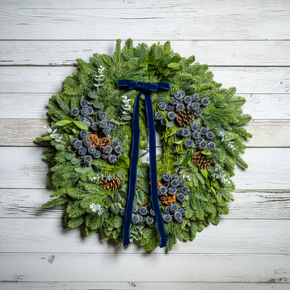 Christmas wreath with greenery, pinecones, and a blue ribbon on a wooden background
