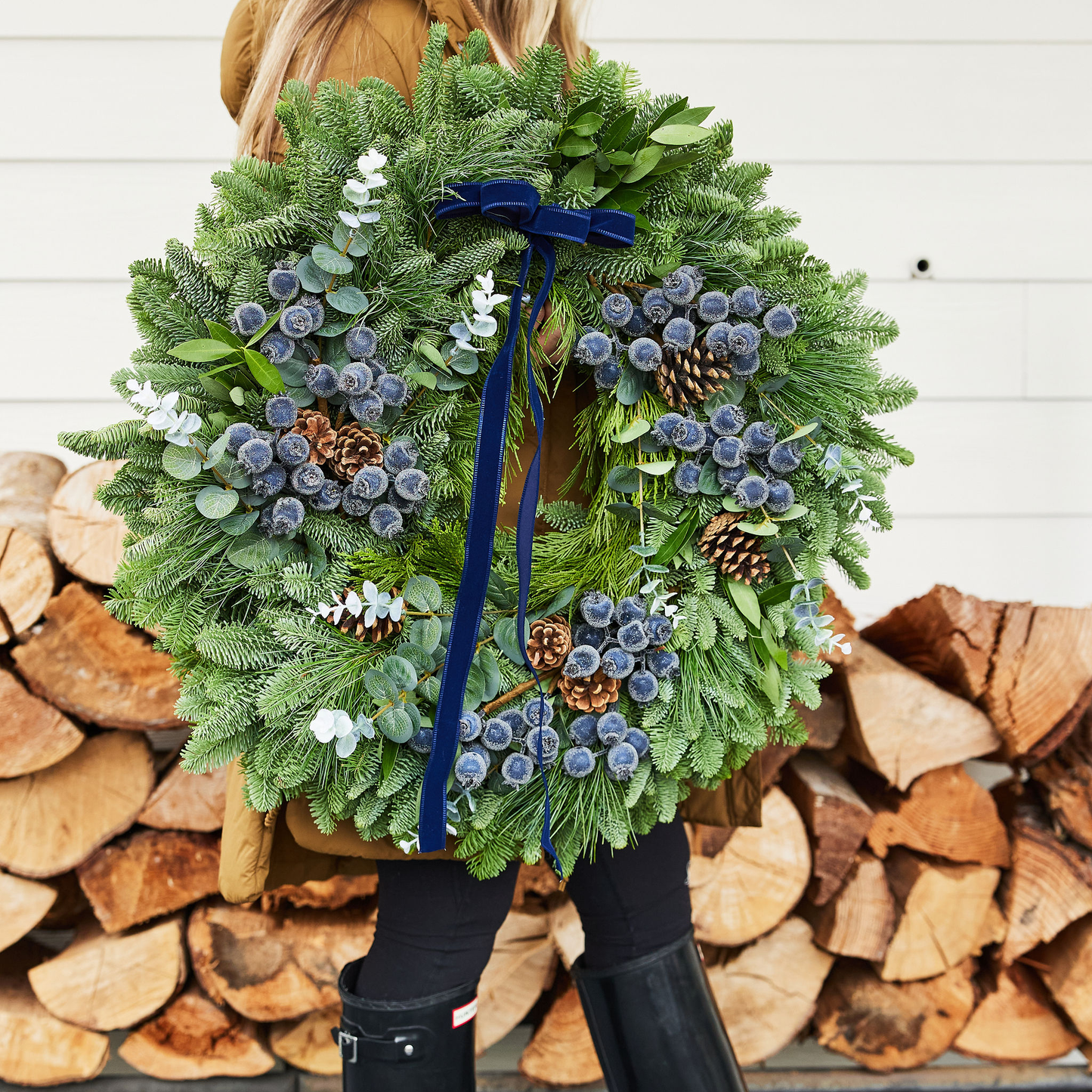 Person holding a large green wreath with decorative elements against a wooden background