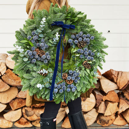 Person holding a large green wreath with decorative elements against a wooden background