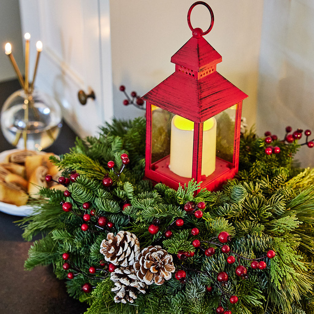 Centerpiece of noble fir, cedar, red berry branches, frosted pine cones, red LED lantern