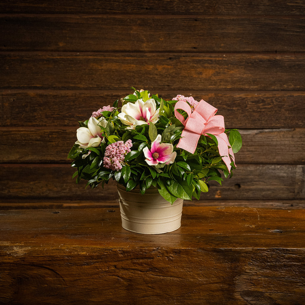 Fresh salal and green huckleberry with faux magnolia flowers, faux pink verbena, and a mauve pink bow in a white metal pot